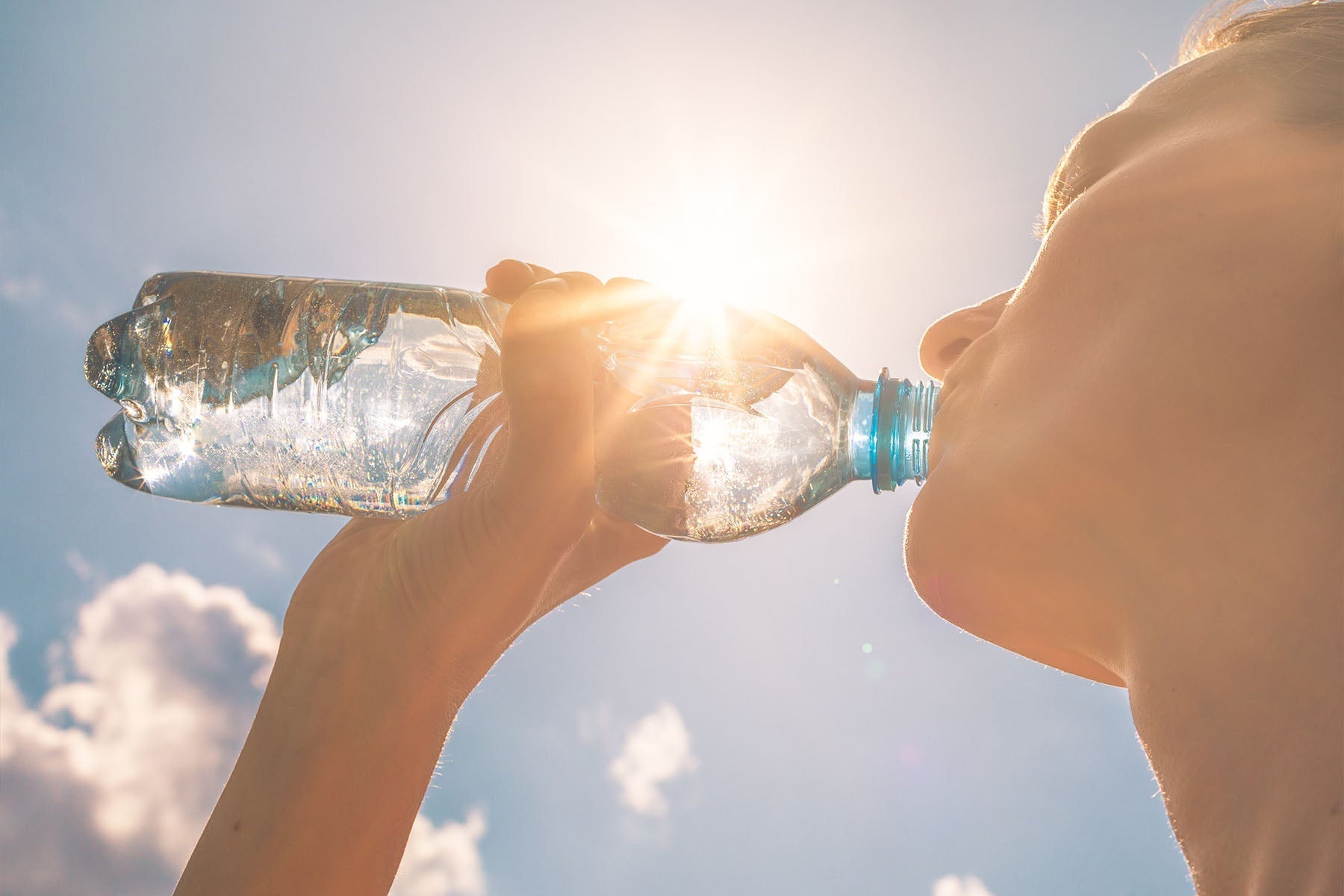 Woman drinking water from a bottle under bright sunlight